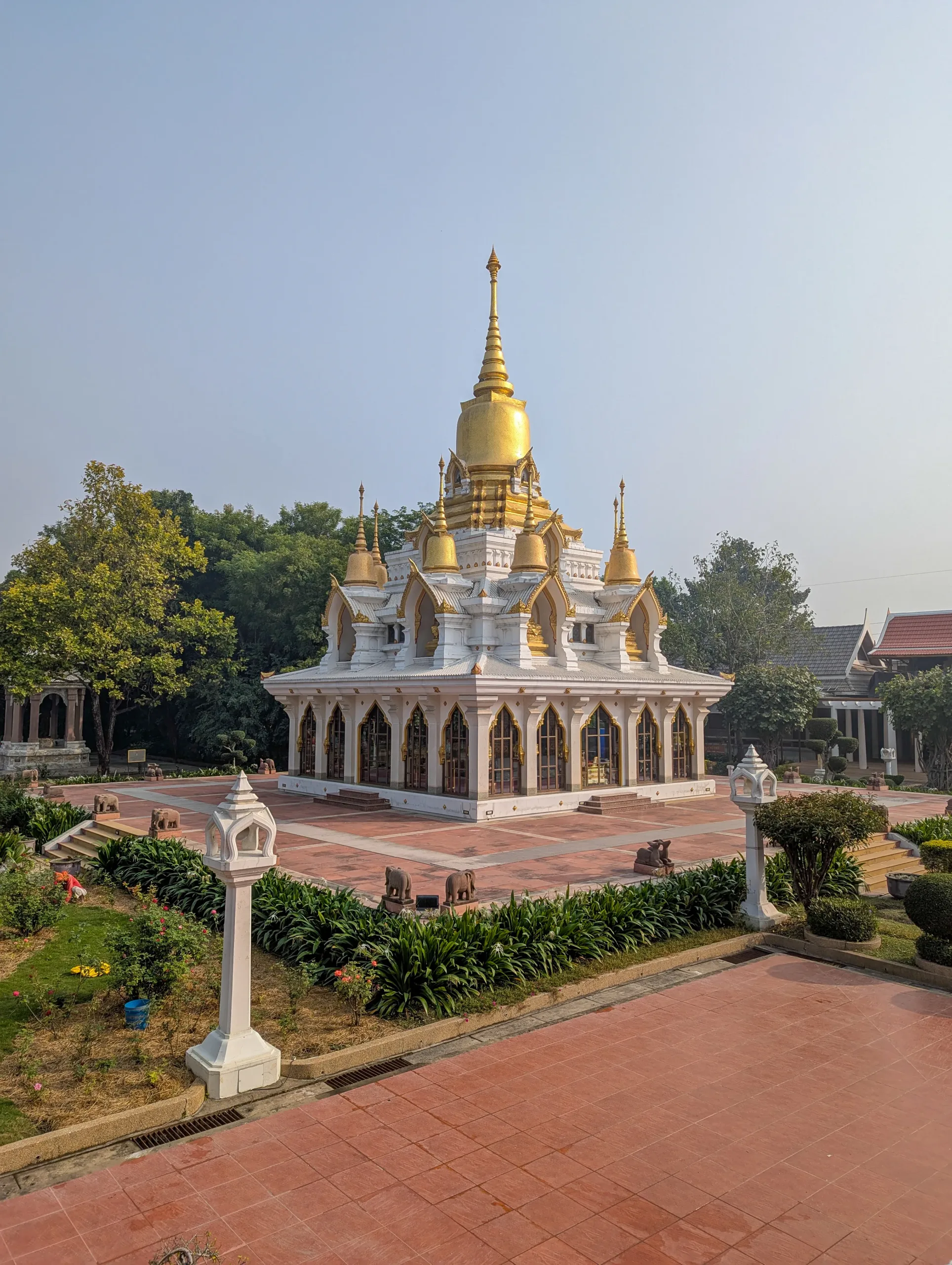 Elegant white and gold shrine with ornate spires and pointed arches at Wat Thai Temple in Kushinagar, surrounded by decorative gardens and lantern posts.