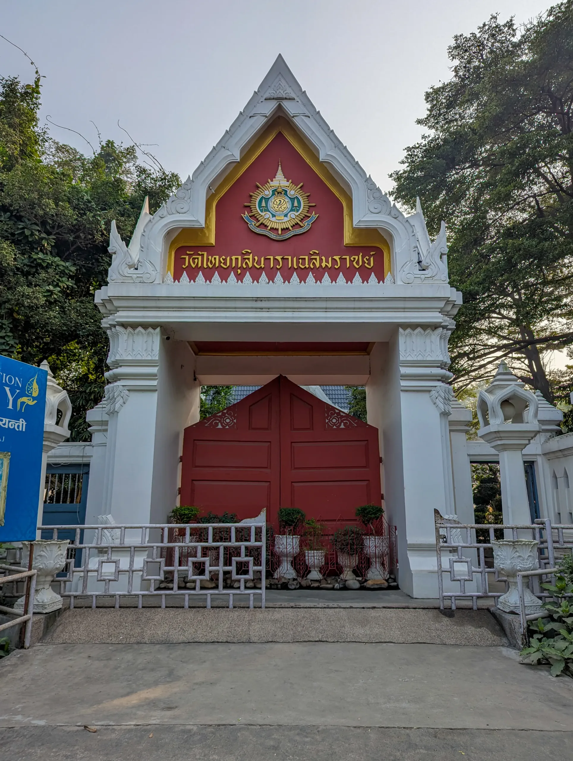 Ornate Thai-style entrance gate of Wat Thai Temple in Kushinagar with a red door, white gabled arch, and gold-accented inscription.