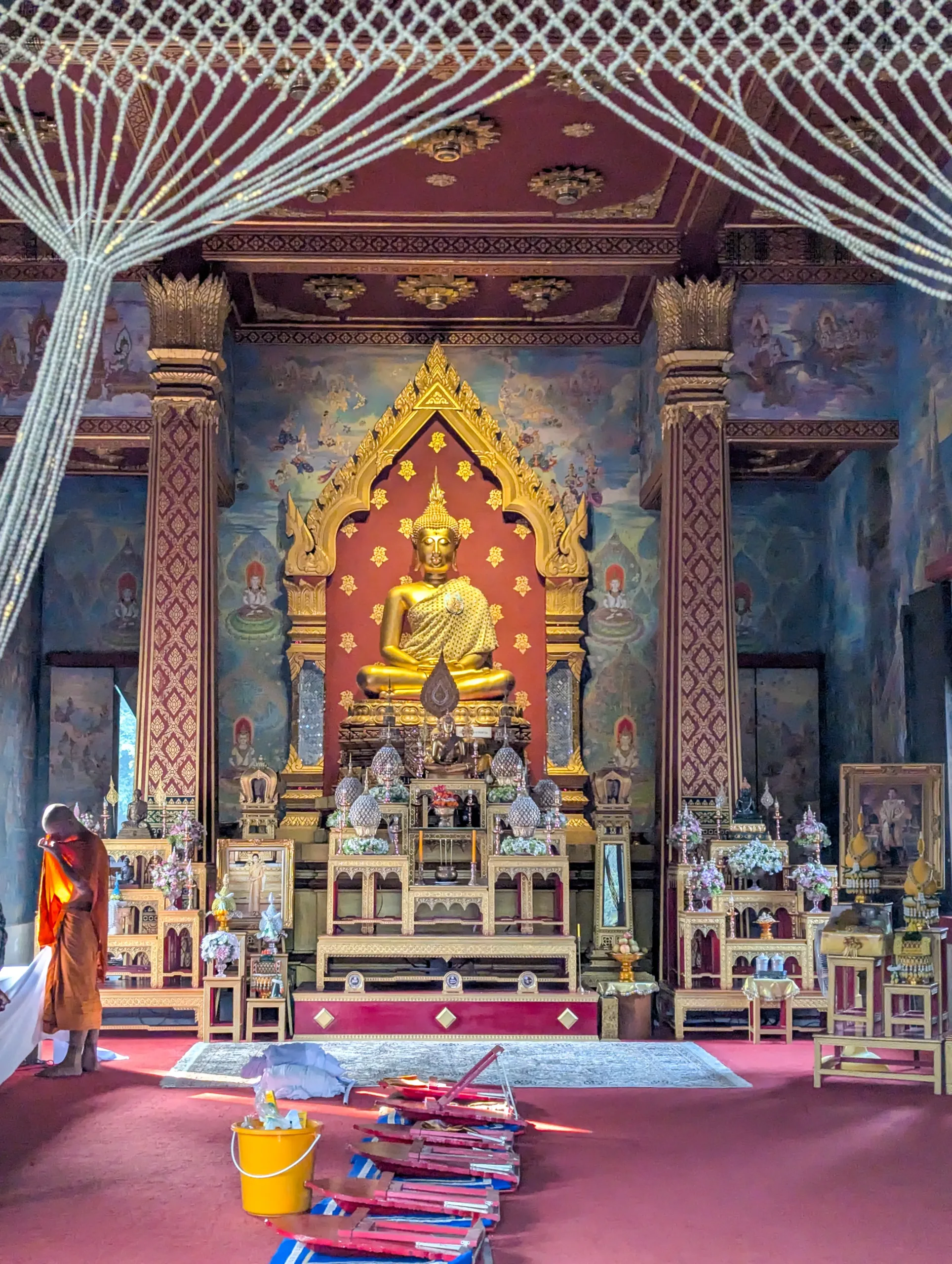 Ornate golden Buddha statue on an elaborate altar inside Wat Thai Temple in Kushinagar, with richly patterned pillars, murals, and devotional offerings.