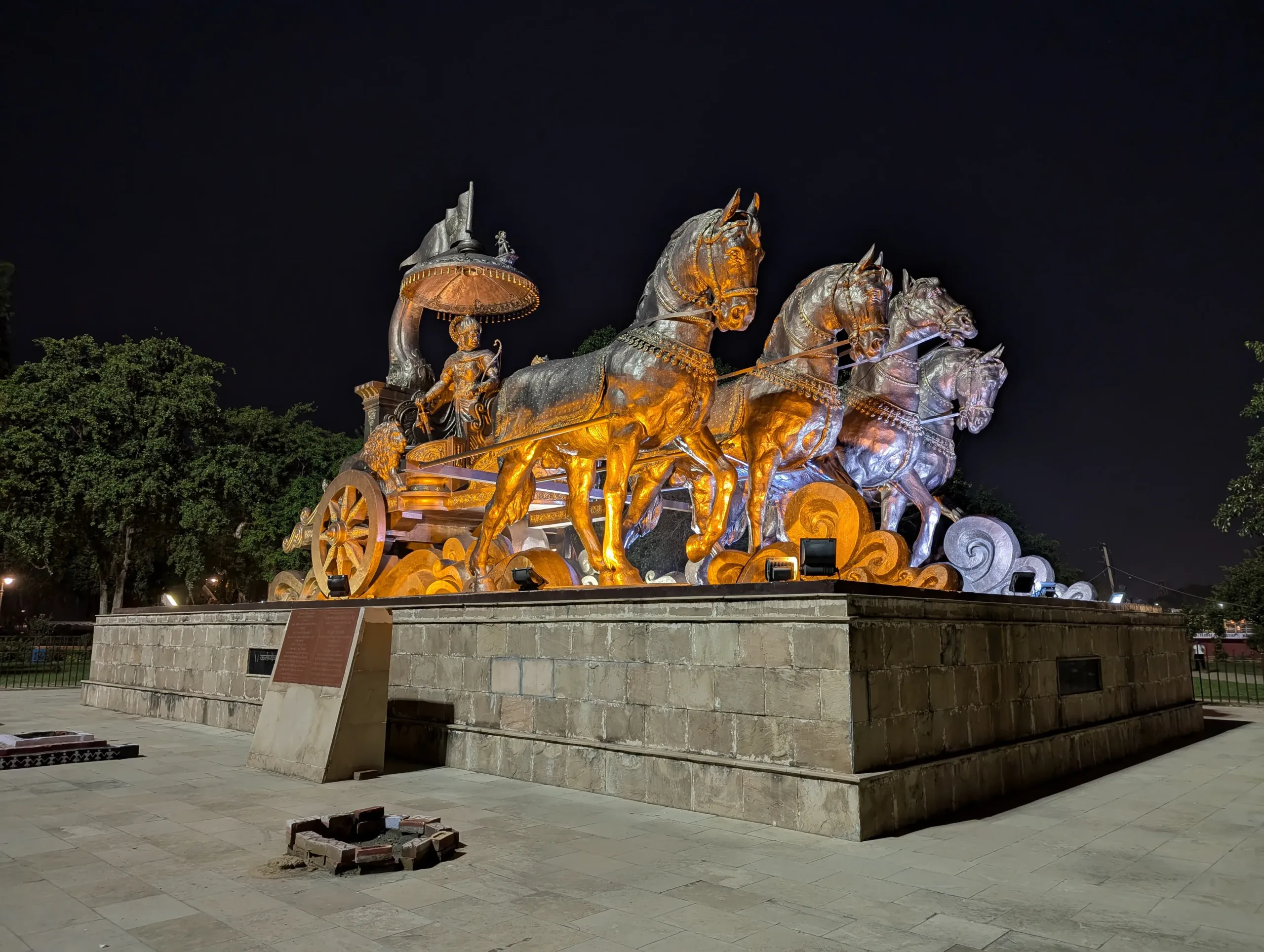 Angled night view of the illuminated bronze chariot statue of Krishna and Arjuna with four horses at Brahma Sarovar in Kurukshetra