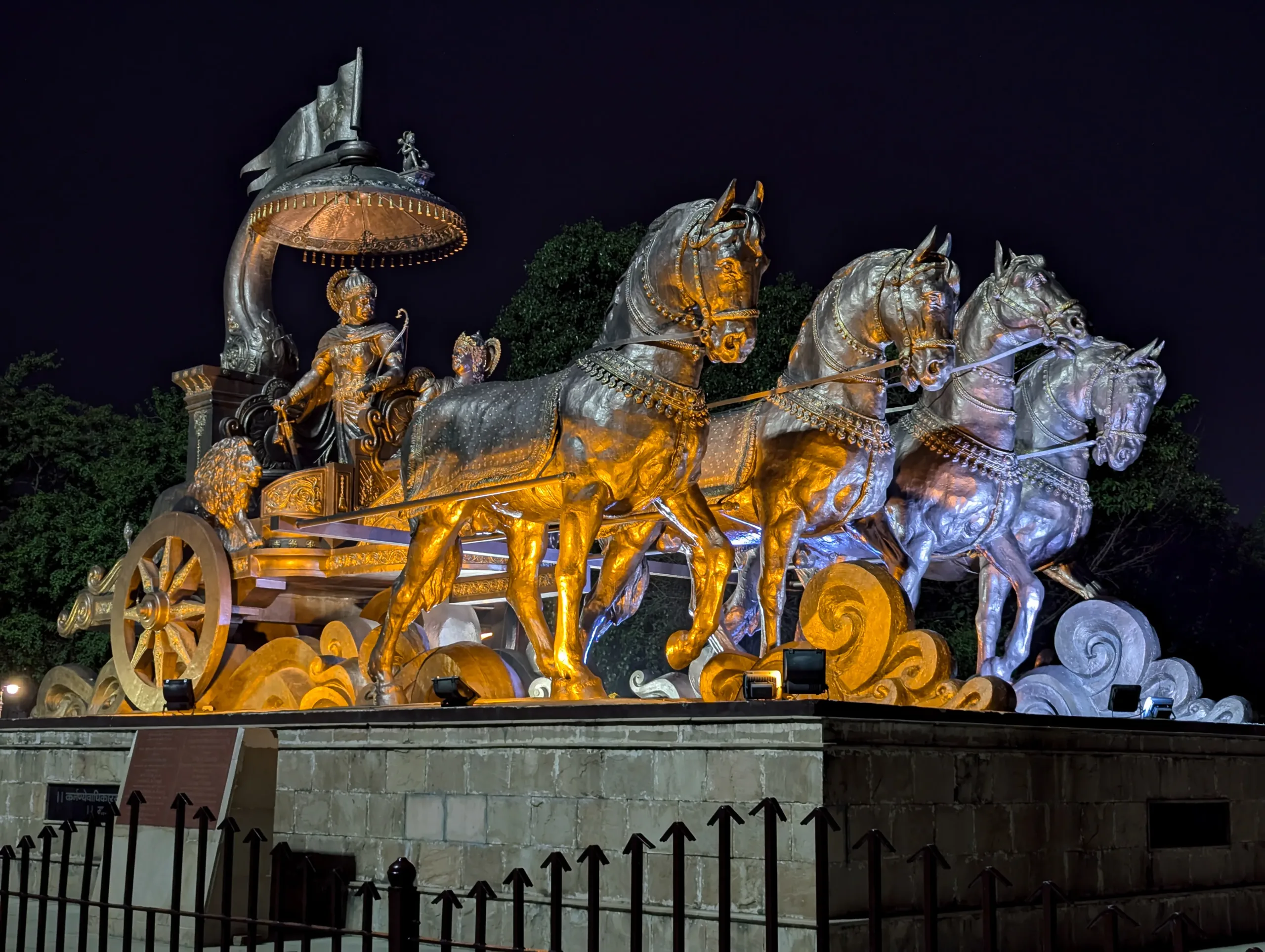 Side‑lit night view of the bronze chariot statue of Krishna and Arjuna with four horses at Brahma Sarovar in Kurukshetra