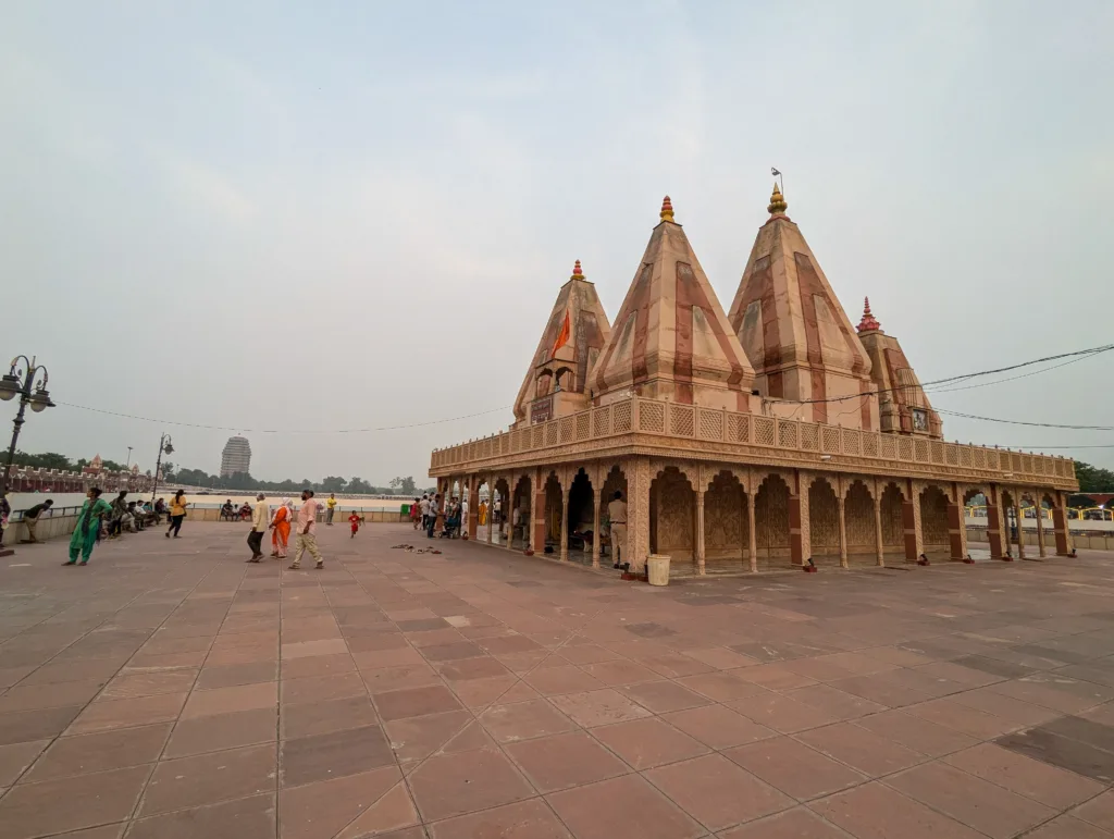 Wide courtyard with pilgrims around the Sarveshwar Mahadev Temple at Brahma Sarovar in Kurukshetra, showing pink shikharas and carved arcade