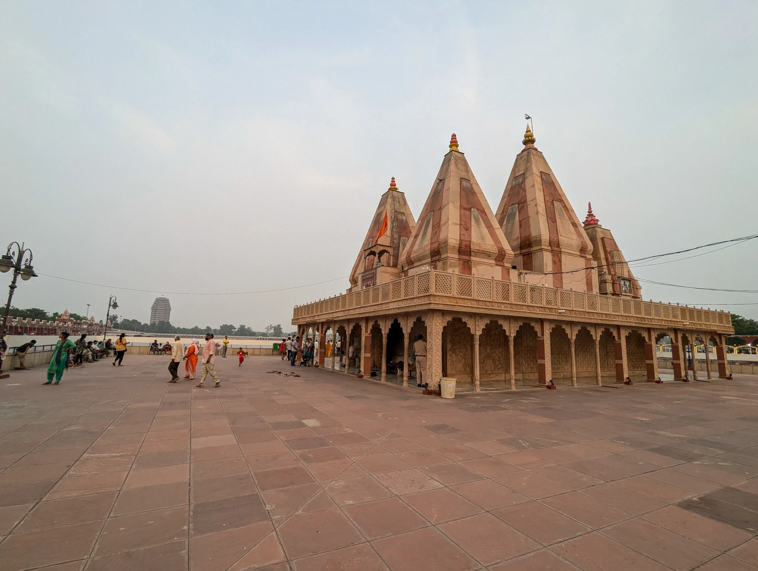 Wide courtyard with pilgrims around the Sarveshwar Mahadev Temple at Brahma Sarovar in Kurukshetra, showing pink shikharas and carved arcade
