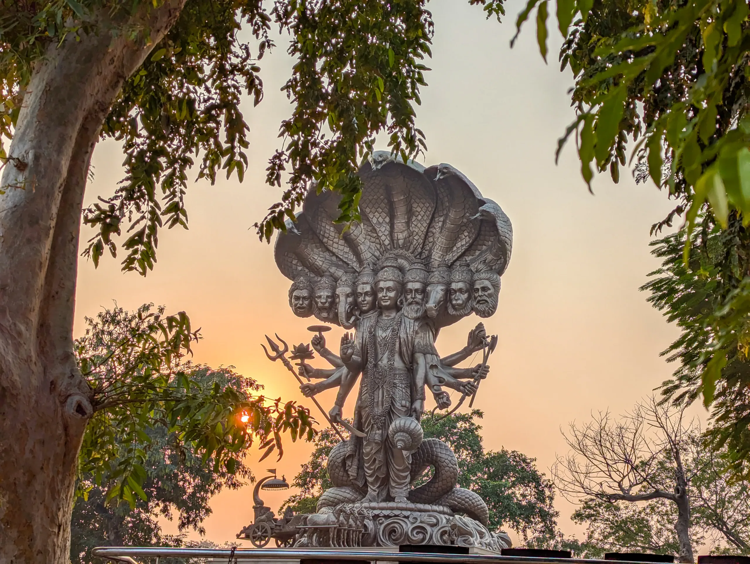Virat Swaroop statue of Lord Krishna beneath the Sheshnag hood at Jyotisar, Kurukshetra, framed by trees at sunset
