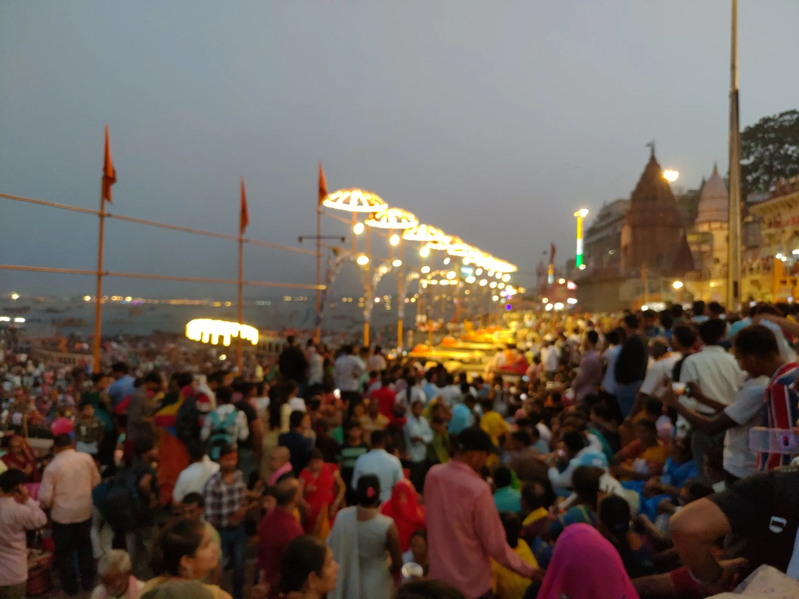 Evening view of the Ganga Aarti at Dashashwamedh Ghat in Banaras, with glowing canopies, priests on the platform, and a large crowd gathered along the river steps