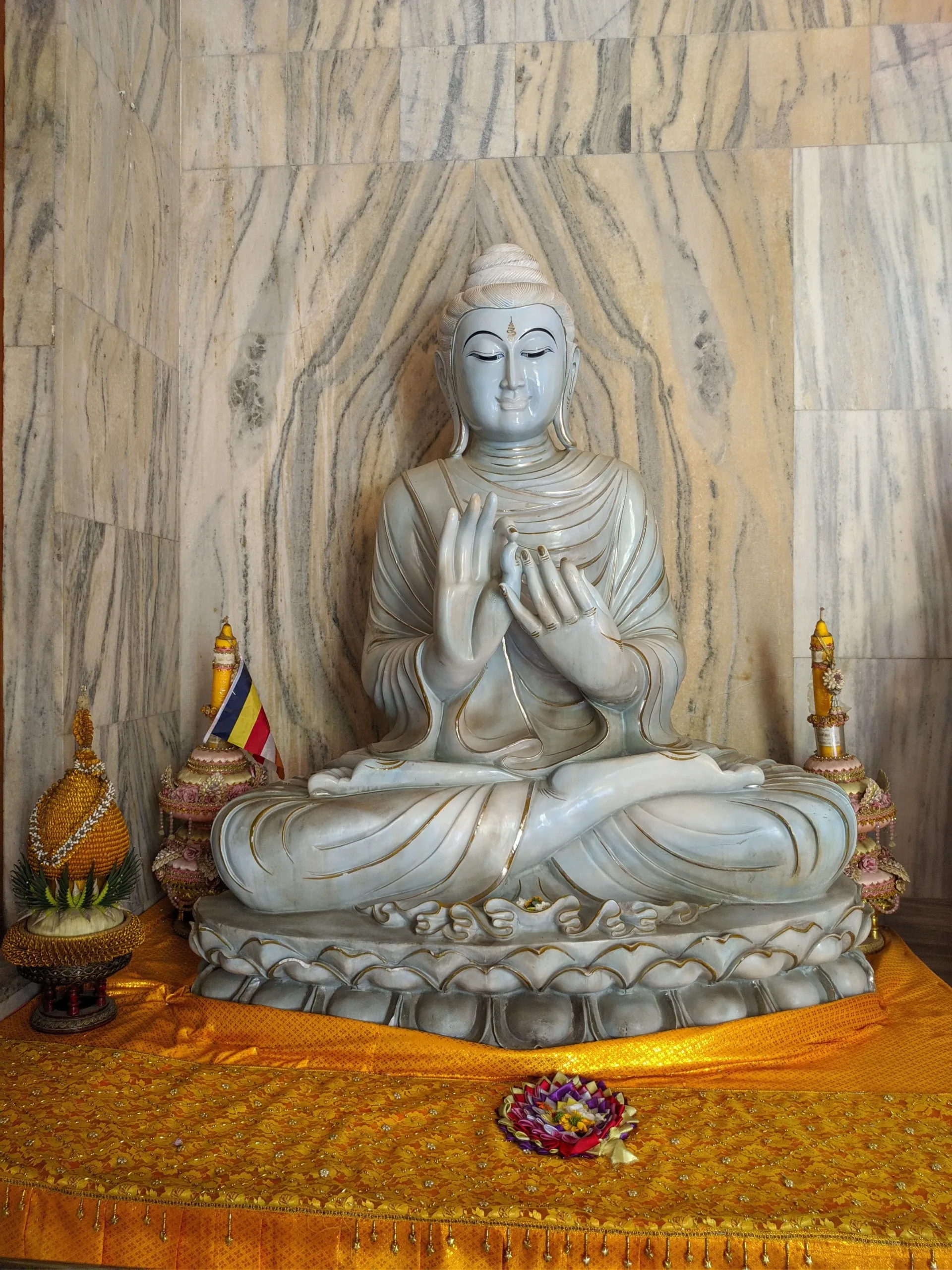 Front view of a serene marble Buddha statue seated on a lotus pedestal inside the Mulagandha Kuti Vihar temple at Sarnath near Banaras, with offerings and gold cloth on the altar